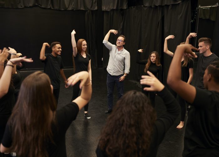 Teacher With Male And Female Drama Students At Performing Arts School In Studio Improvisation Class