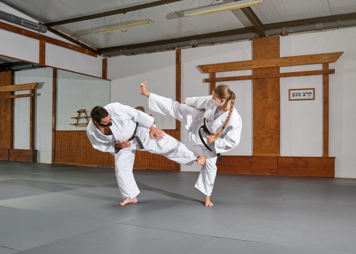 Two people with mask and kimono practicing krav maga kicks in a